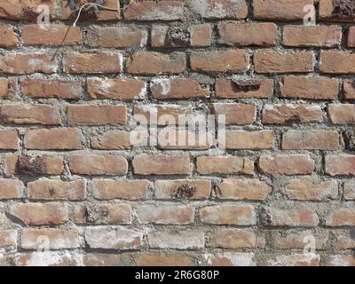 A bright red fire hydrant with a metal bar handle is prominently situated against a textured, brick wall background Stock Photo