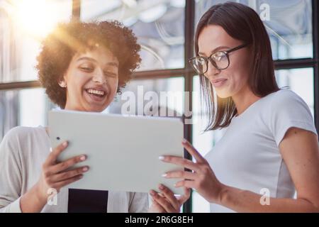 Cheerful female employees enjoying break. Two women in formal clothes sitting in office lounge, chatting and laughing Stock Photo