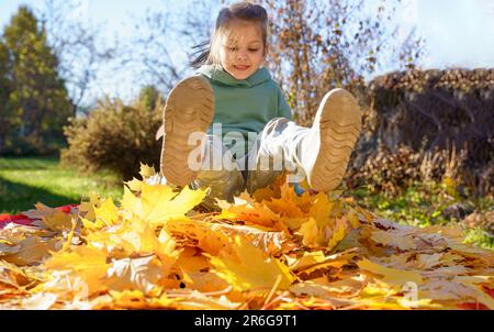 Girl kid jumping on trampoline with autumn leaves. Bright yellow orange maple foliage. Child walking, having fun, playing in fall backyard. Outdoor fu Stock Photo