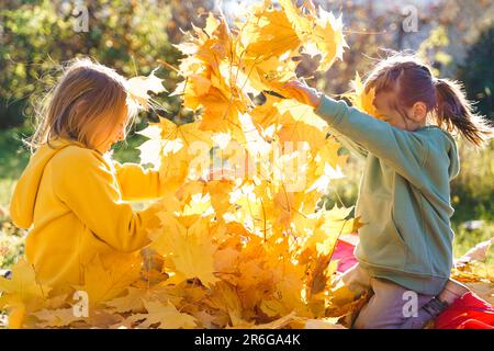 Girls kids playing jumping on trampoline with autumn leaves. Bright yellow orange maple foliage. Children walking, having fun in fall backyard. Outdoo Stock Photo