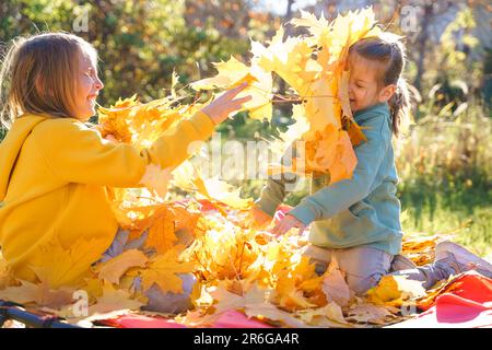 Girls kids playing jumping on trampoline with autumn leaves. Bright yellow orange maple foliage. Children walking, having fun in fall backyard. Outdoo Stock Photo