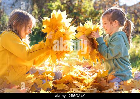 Girls kids playing jumping on trampoline with autumn leaves. Bright yellow orange maple foliage. Children walking, having fun in fall backyard. Outdoo Stock Photo