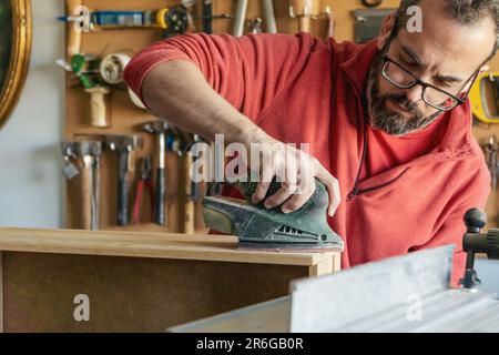 Carpenter with glasses using electric sander at his workshop Stock Photo