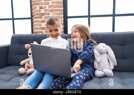 Adorable girls using laptop sitting on sofa at home Stock Photo