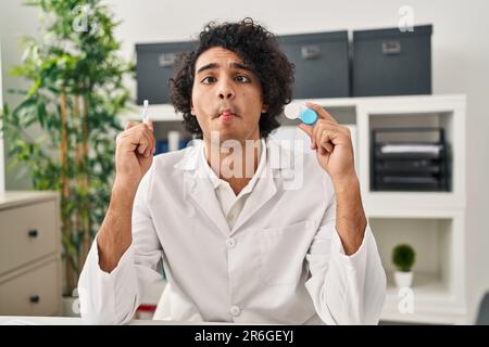 Hispanic man with curly hair holding contact lenses making fish face with mouth and squinting eyes, crazy and comical. Stock Photo