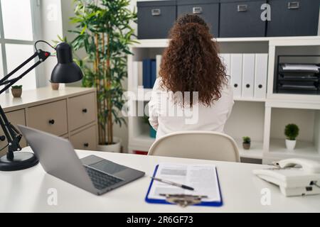 Young hispanic woman wearing doctor uniform and stethoscope standing backwards looking away with crossed arms Stock Photo