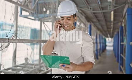 Young hispanic man architect talking on holding clipboard at street Stock Photo
