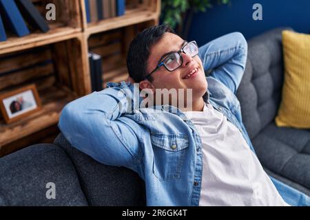 Down syndrome man relaxed with hands on head sitting on sofa at home Stock Photo