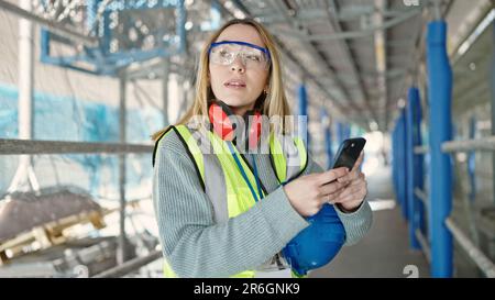 Young blonde woman builder using smartphone at street Stock Photo