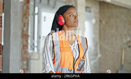 African american woman builder wearing headphones for noise at construction site Stock Photo