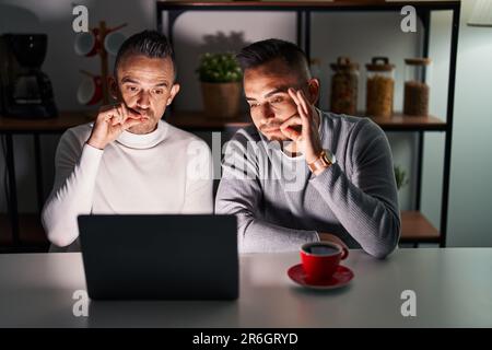Homosexual couple using computer laptop mouth and lips shut as zip with fingers. secret and silent, taboo talking Stock Photo