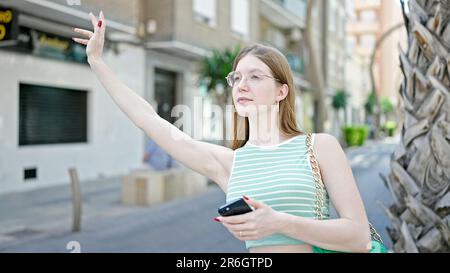 Young blonde woman using smartphone asking for taxi at street Stock Photo