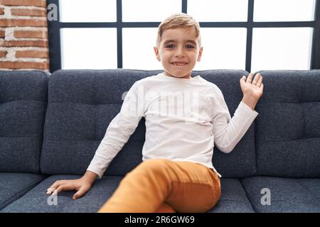 Adorable hispanic boy saying hello with hand sitting on sofa at home Stock Photo