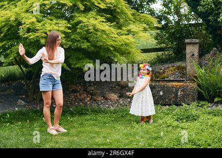 Young mother dancing with cute little daughter in garden, family spending time together Stock Photo