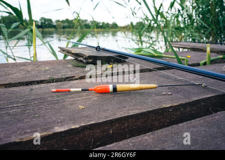 Fishing float, fishing bobber on the wooden pier. Fishing rod and fishing equipment on the jetty at the lake in the forest. Fishing concept. Stock Photo
