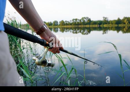 Fisherman holding fishing rod at the lake. Fishing. Closeup of hand holding fishing rod and fishing reel. Stock Photo