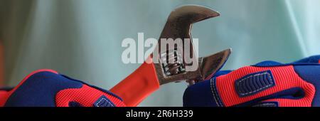 Person hands in protective work gloves holding spanner. Stock Photo