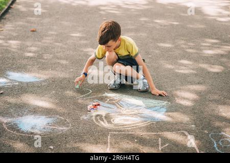 Child drawing with chalk outside in the park on nice sunny day Stock Photo