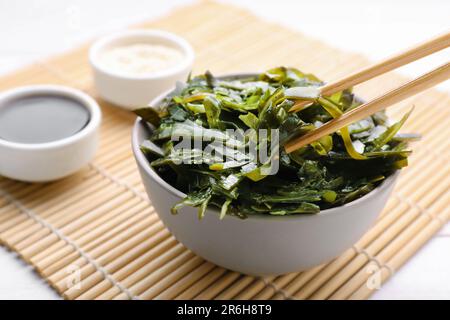 Fresh laminaria (kelp) seaweed in bowl and chopsticks on white table Stock Photo