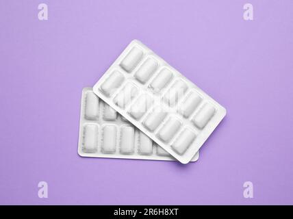 Blisters with chewing gums on violet background, flat lay Stock Photo