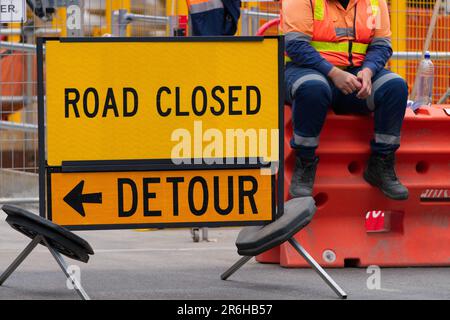 Metal yellow background road closed detour sign indicating construction on road, Victoria, Australia.