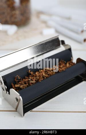 Roller with tobacco on white wooden table, closeup. Making hand rolled cigarettes Stock Photo