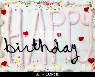 Happy Birthday text on white cake frosting with red hearts and colorful sprinkles Stock Photo