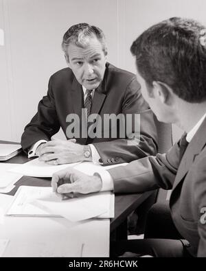 1960s TWO MEN IN A SERIOUS DISCUSSION AT DESK WITH SEVERAL PAPERS AND FOLDERS MATURE MAN LOOKING AT YOUNGER MAN SEEN FROM BEHIND - o2628 HAR001 HARS CONFIDENCE MIDDLE-AGED B&W MIDDLE-AGED MAN SUIT AND TIE MENTOR OCCUPATION HEAD AND SHOULDERS AND CAREERS LEADERSHIP REAR VIEW OPPORTUNITY FOLDERS MENTORING OCCUPATIONS CONNECTION CONCEPTUAL FROM BEHIND SINCERE SOLEMN AGE DIFFERENCE BACK VIEW FOCUSED INTENSE SEVERAL YOUNG ADULT MAN YOUNGER BLACK AND WHITE CAREFUL CAUCASIAN ETHNICITY EARNEST HAR001 INTENT OLD FASHIONED POSTERIZED Stock Photo