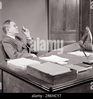 1950s BUSINESS MAN SMOKING A CIGARETTE RELAXED WITH HIS FEET UP ON THE DESK LOST IN THOUGHT - o338 HAR001 HARS B&W MIDDLE-AGED MAN CIGARETTES SUIT AND TIE DREAMS HIS TOBACCO STRATEGY RELAXED REFLECTIVE THINK BAD HABIT OCCUPATIONS REFLECTING SMOKER NICOTINE PONDER PONDERING BOSSES CONSIDER LOST IN THOUGHT ADDICTIVE ESCAPE CONTEMPLATIVE MEDITATE LOOKING UP MANAGERS MEDITATIVE RELAXATION SOLUTIONS BLACK AND WHITE CAUCASIAN ETHNICITY CONSIDERING HAR001 OLD FASHIONED Stock Photo