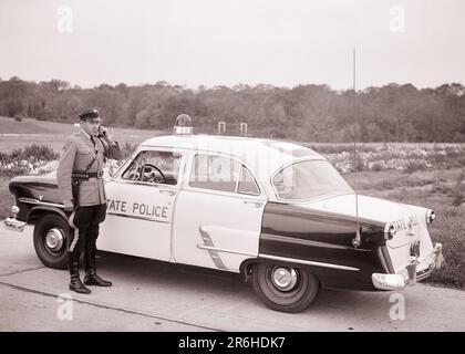 1950s NJ STATE POLICE PATROL CAR TROOPER USING MOBILE PHONE TALK TO HEADQUARTERS OTHER CARS OR OVERHEAD AIRPLANE NEW JERSEY USA - q54353 CPC001 HARS CAREER SERVE VEHICLE SECURITY TECHNOLOGY SAFETY INFORMATION FORD LIFESTYLE OVERHEAD JOBS COMMUNICATING COPY SPACE FULL-LENGTH HIGHWAY PERSONS INSPIRATION AUTOMOBILE MALES ORDER OFFICER PROFESSION CONFIDENCE TRANSPORTATION B&W COP SKILL OCCUPATION PROTECT SKILLS HIGH ANGLE ADVENTURE AND AUTOS CAREERS EXTERIOR LEADERSHIP PROGRESS PRIDE OPPORTUNITY AUTHORITY OCCUPATIONS PHONES UNIFORMS USING CONNECTION PATROL CONCEPTUAL TELEPHONES AUTOMOBILES Stock Photo