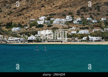 Ios, Greece - May 16, 2021 : Young tourists enjoying standup paddle boarding at the famous beach of Mylopotas Ios Greece Stock Photo