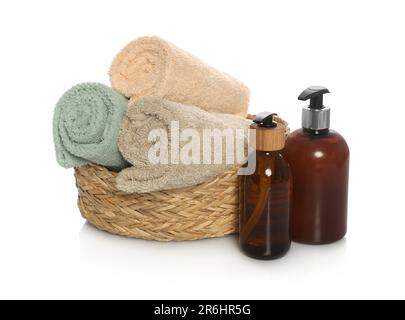 Soft towels in wicker basket and bottles of cosmetic products on white background Stock Photo