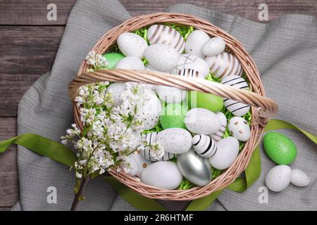 Easter eggs in basket and lilac flowers on wooden table, flat lay Stock Photo