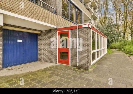 a red and blue door in front of a grey brick building with white trim on the side of the building Stock Photo