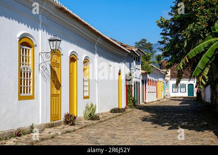 Typical cobblestone street with colorful colonial buildings and trees in the late afternoon sun in historic town Paraty, Brazil Stock Photo
