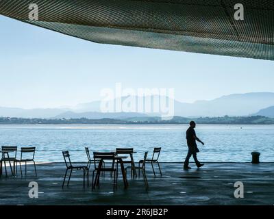 Silhouettes of people walking along a quay in the port of Santander. Stock Photo