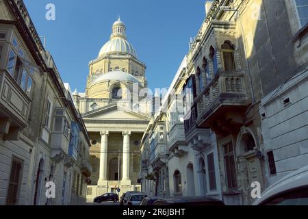 Basilica of Christ the King and traditional closed wooden balconies (gallarija) in a street of Paola, Malta Stock Photo