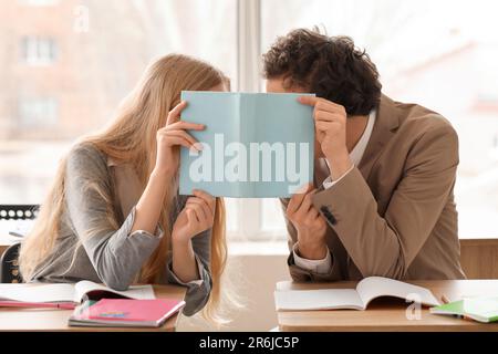 Teenage couple covering themselves with book in classroom Stock Photo