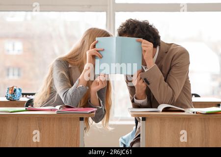 Teenage couple covering themselves with book in classroom Stock Photo