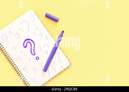 Notebook with drawn question marks and marker on yellow background Stock Photo