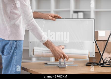 Young man wrapping computer monitor with stretch film in office Stock ...