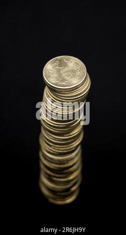 top view perspective of shiny gold indian 5 or five rupee coins stacked up to form a tall tower isolated in a black background Stock Photo