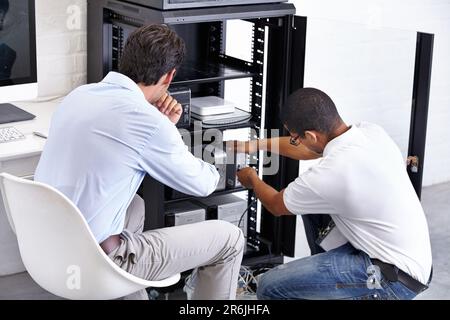 Server room, man and technician working with electronics for hardware maintenance of glitch in office. IT support, worker and electrical engineer Stock Photo