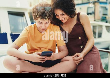 A heartwarming scene as a mother and her son share laughter and joy. The boy shows his mother something amusing on a mobile phone, creating a special Stock Photo
