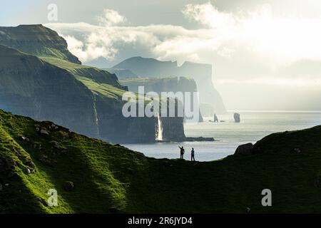 Silhouette of hikers admiring cliffs standing on top of mountain ridge above the ocean, Kalsoy island, Faroe Islands, Denmark, Europe Stock Photo