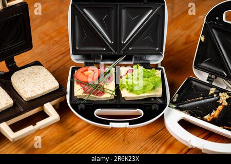 a variety of sandwiches that can be prepared in a sandwich maker concept. Row of electric sandwich makers on a wooden background. Stock Photo