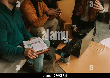 Three multiracial colleagues discussing statistics and teamwork results while having coffee time at the coffee bar Stock Photo