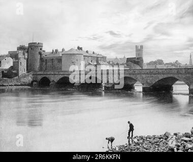 A late 19th century view of people fishing beside the  Thomond Bridge built in 1836 and beyond is 13th-century King John's Castle, aka Limerick Castle, Ireland. Although the site dates back to 922 when the Vikings lived on the Island, the castle itself was built on the orders of King John in 1200. One of the best preserved Norman castles in Europe, the walls, towers and fortifications remain today. Stock Photo