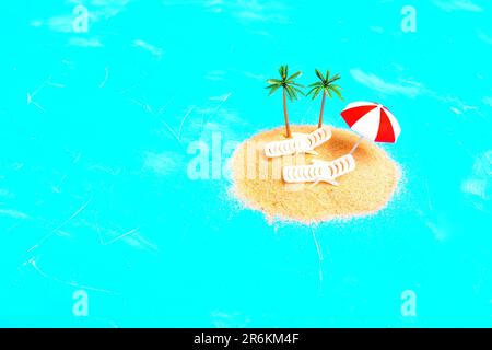 Small mound of sand forms the beach isolated on blue background, adorned with a pair of toy beach loungers and toy palm trees capturing the essence of Stock Photo