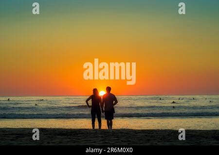 Couple hold hands on Guiones Beach where people gather to surf and watch at sunset, Playa Guiones, Nosara, Guanacaste, Costa Rica, Central America Stock Photo